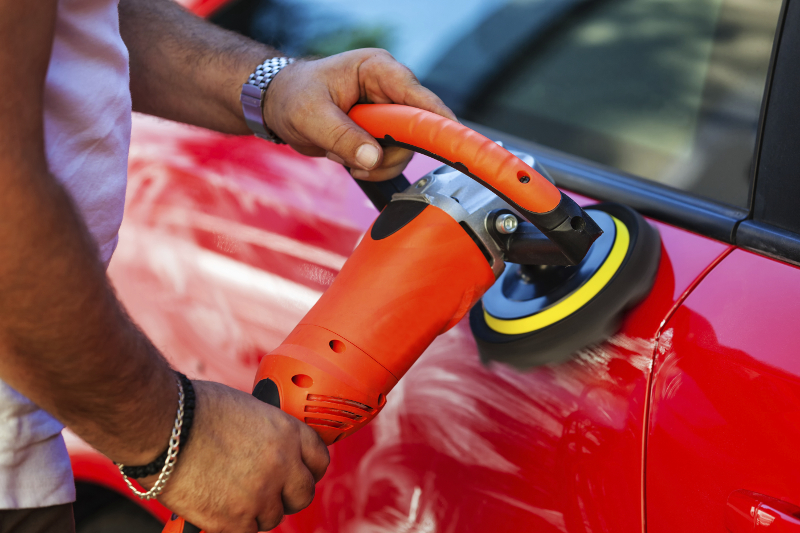 A technician polishing the paint of a red car